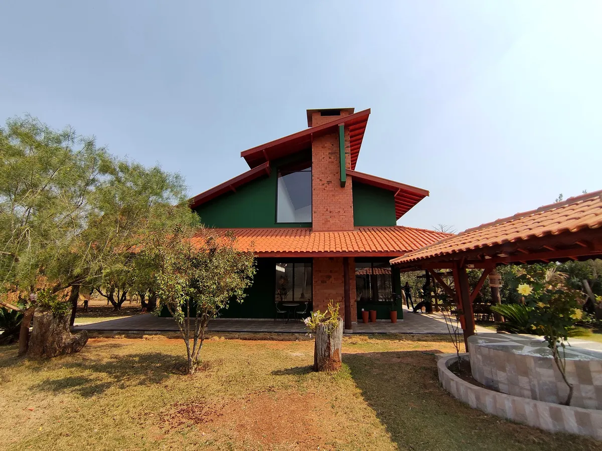 Casa de campo com chaminé em tijolo aparente, paredes verdes e telhado cerâmico