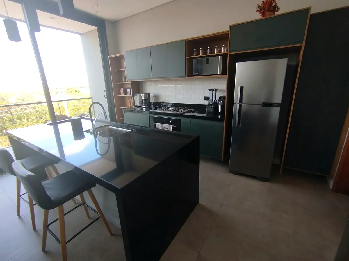 Cozinha com armários verdes, ilha em granito preto e vista pela janela