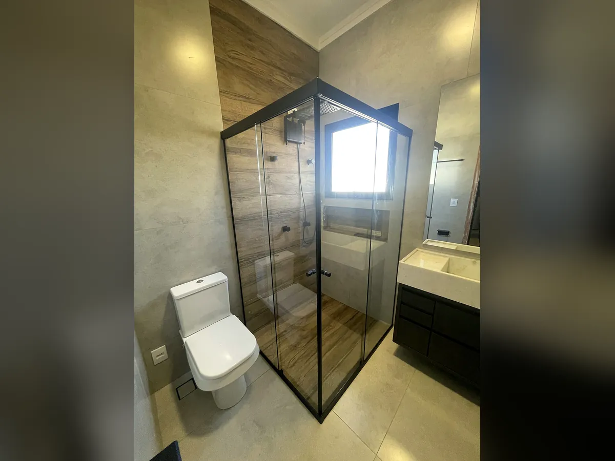 Banheiro com box de vidro, revestimento amadeirado e bancada escura
