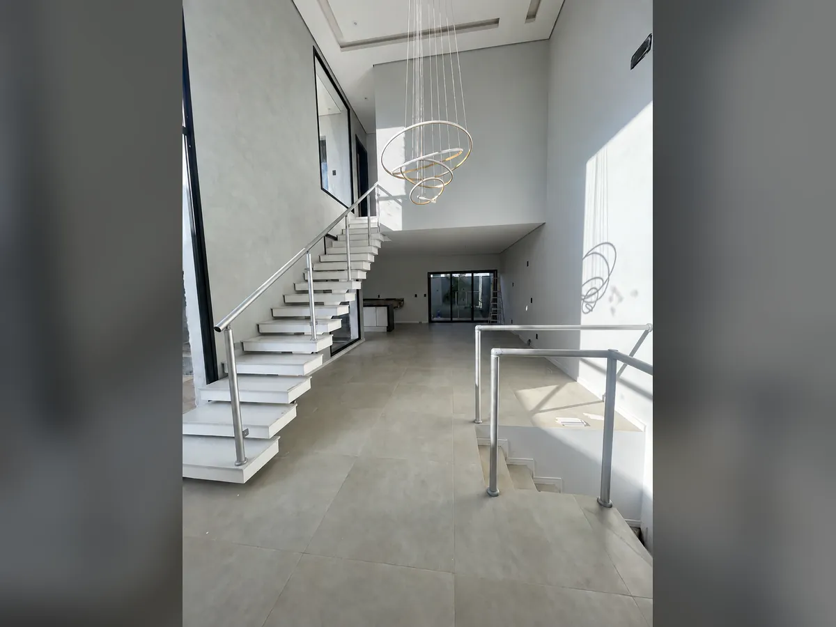 Sala com pé-direito duplo, escada branca e lustre pendente