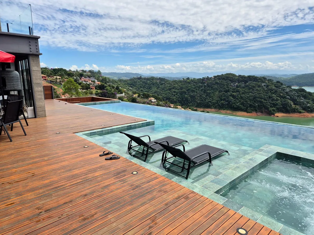 Piscina de borda infinita com deck de madeira e vista para a represa